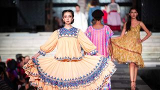 A model walks through a Mexico City fashion show, holding a dress with Indigenous design with both hands